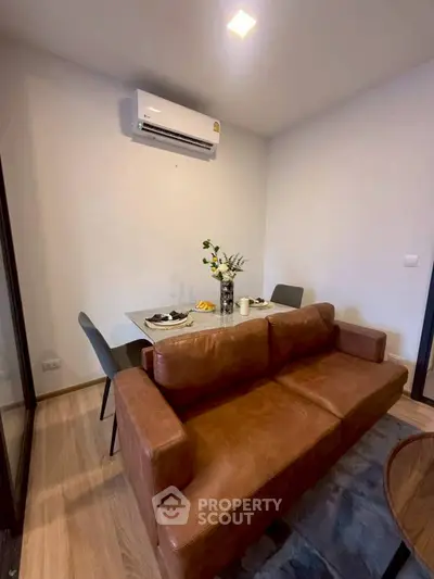 Cozy living room with leather sofa and dining table, featuring modern air conditioning.