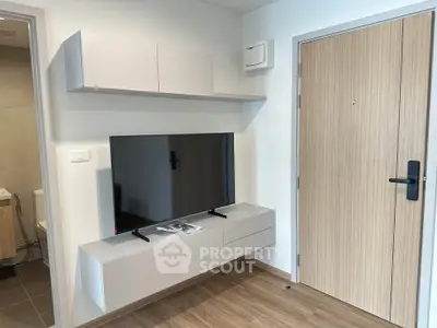 Modern living room with sleek TV setup and wooden flooring, adjacent to a stylish bathroom entrance.