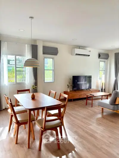 Modern living room with wooden dining set and large windows offering natural light.