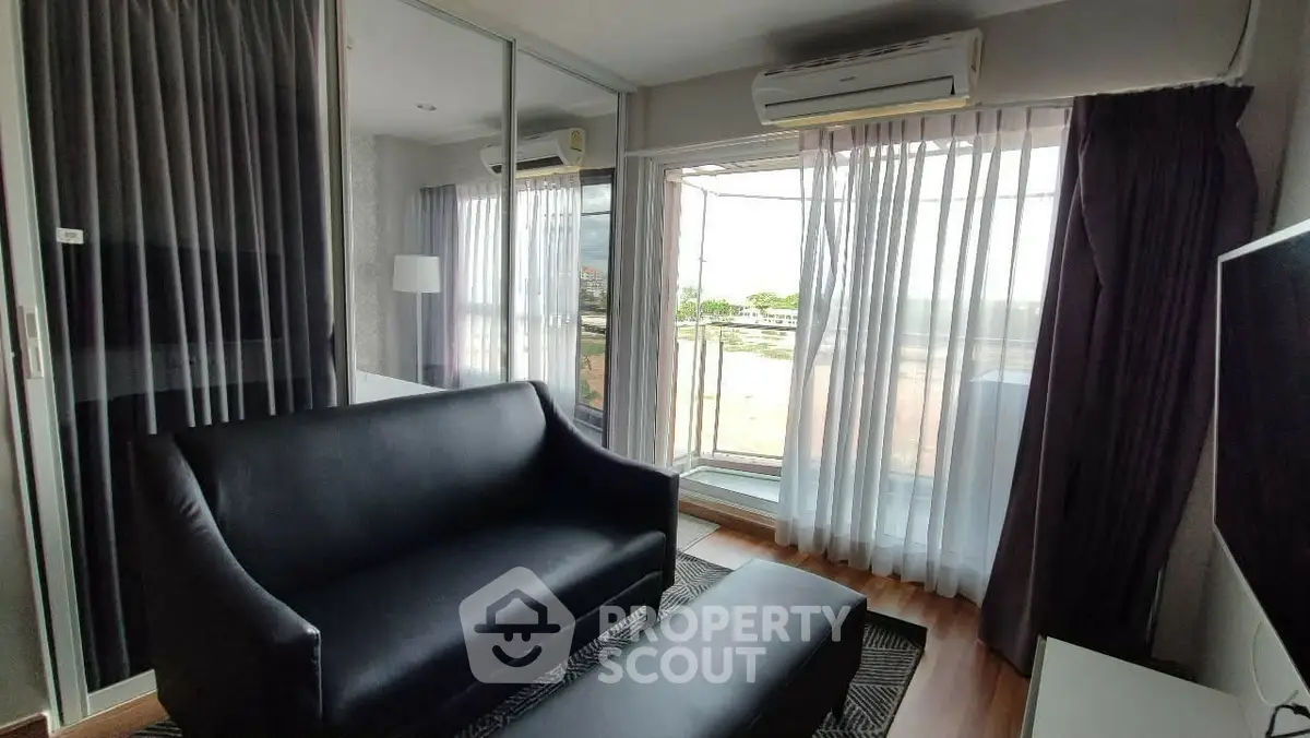 Modern living room with black sofa and large windows offering natural light.
