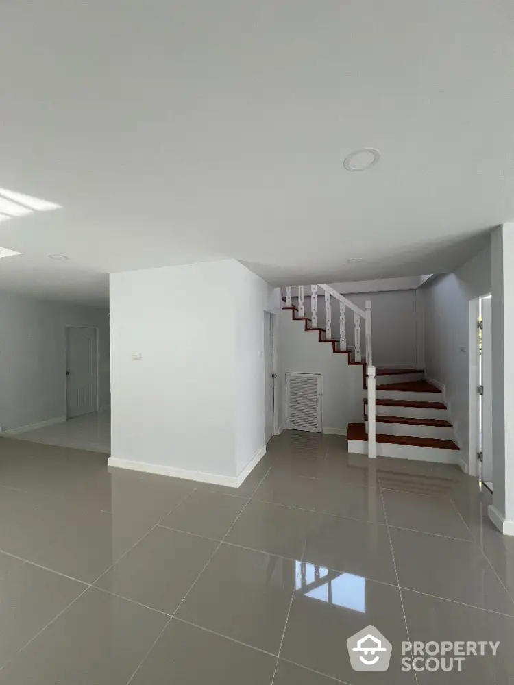 Spacious and bright open-plan living area with glossy tiled flooring and a striking red staircase leading to the upper level, perfect for modern living.