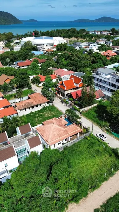 Stunning aerial view of a coastal neighborhood with lush greenery and ocean backdrop, showcasing diverse architecture.