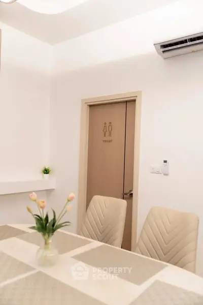 Modern interior with dining area and restroom door, featuring elegant chairs and a vase of tulips.