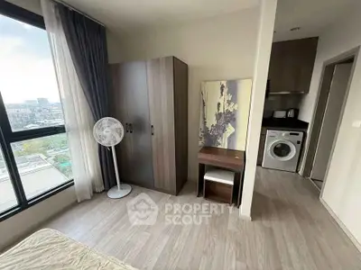 Modern bedroom with city view, featuring wardrobe, fan, and compact kitchen with washing machine.