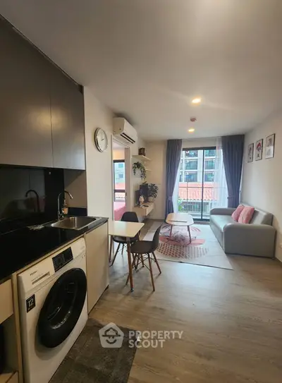Modern living room with open kitchen and washing machine, featuring stylish decor and natural light.