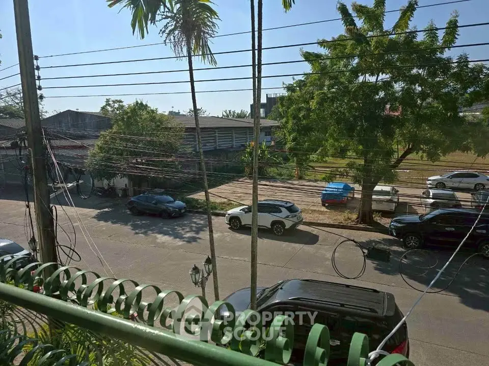 Street view from balcony with parked cars and lush greenery