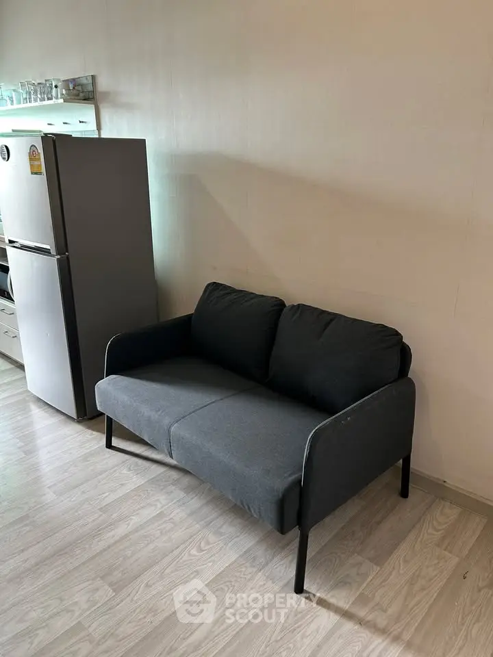 Cozy living room with modern sofa and sleek refrigerator, perfect for compact spaces.