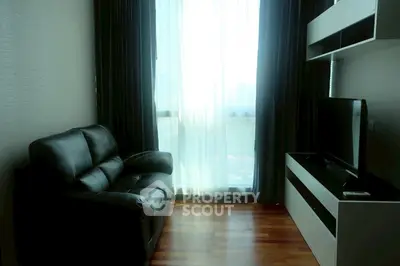 Cozy living room with leather sofa and entertainment unit, featuring large window with sheer curtains.