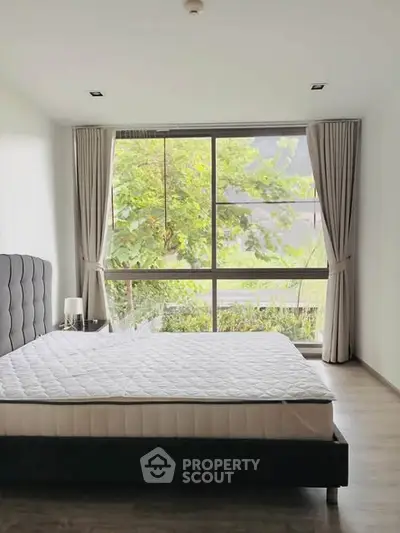 Spacious bedroom with large window offering lush green views, featuring a comfortable bed and elegant curtains.
