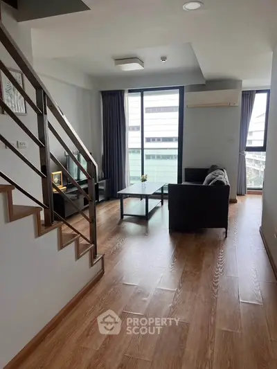 Modern living room with wooden flooring and large windows offering city views.