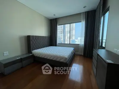 Spacious bedroom with modern furniture and city view, featuring a large window and wooden flooring.