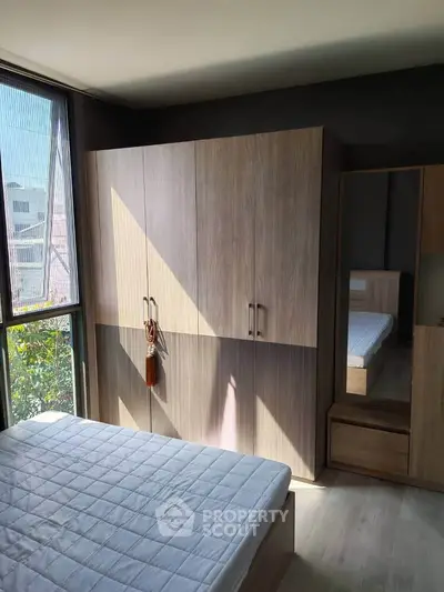 Modern bedroom with large window and wooden wardrobe, perfect for natural light lovers.