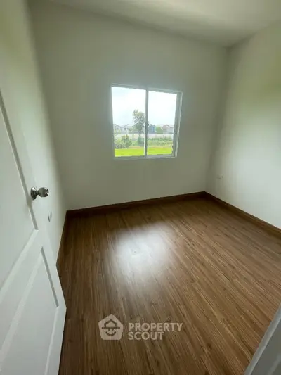 Bright empty bedroom with wooden flooring and large window view