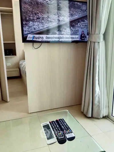 Modern living room with wall-mounted TV and glass coffee table in stylish apartment.
