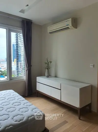 Modern bedroom with air conditioning and city view, featuring sleek furniture and natural light.
