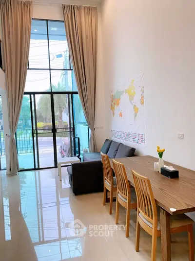 Spacious living room with high ceiling and large windows, modern decor and dining area.