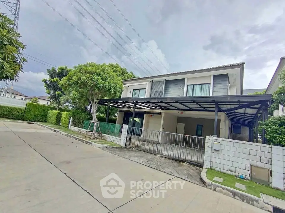 Modern two-story house with carport and lush greenery in a serene neighborhood.