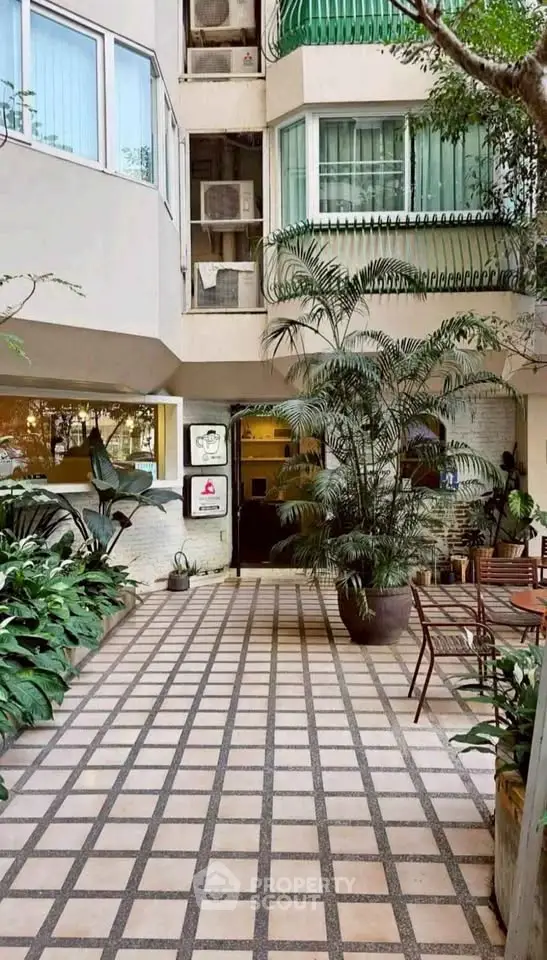 Charming building entrance with lush greenery and outdoor seating area.