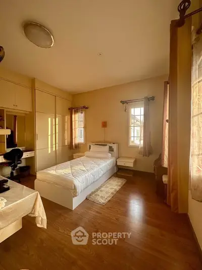 Cozy bedroom with wooden flooring and ample natural light from large windows.