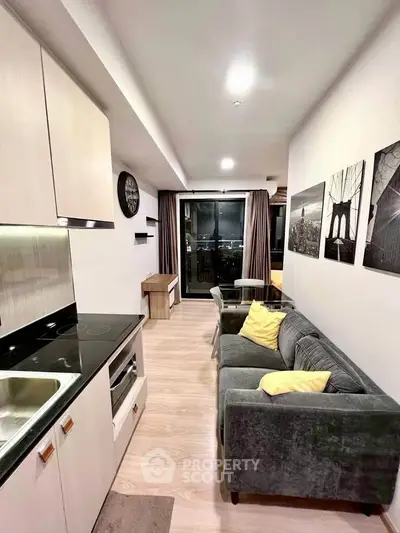 Modern living room with sleek kitchen and city view, featuring stylish decor and cozy seating area.