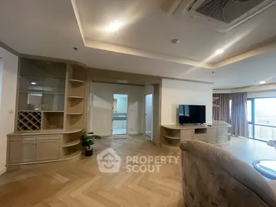 Spacious living room with elegant herringbone wood flooring, custom shelving, and ample natural light from large windows, perfect for entertaining and relaxation.