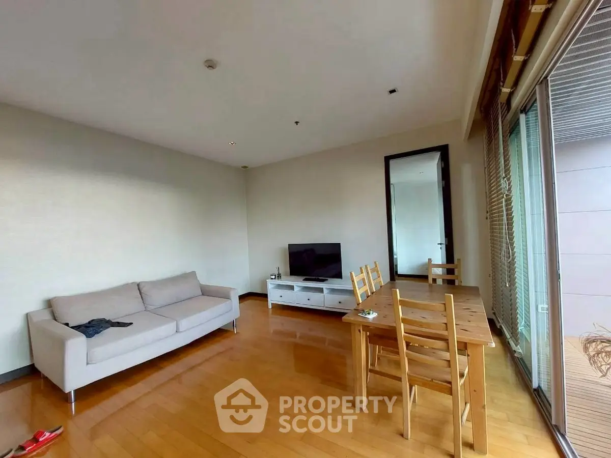 Spacious living room with wooden flooring, cozy sofa, and dining area in modern apartment.