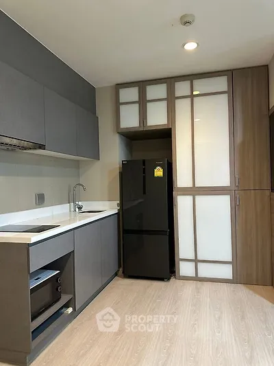 Modern kitchen with sleek cabinetry and black fridge in a compact layout.