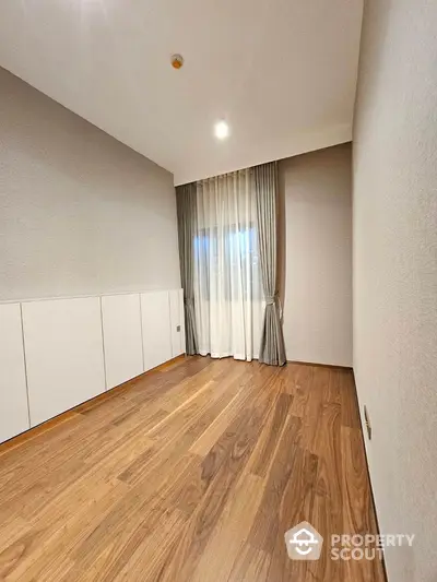 Spacious empty room with wooden flooring and large window, perfect for customization.