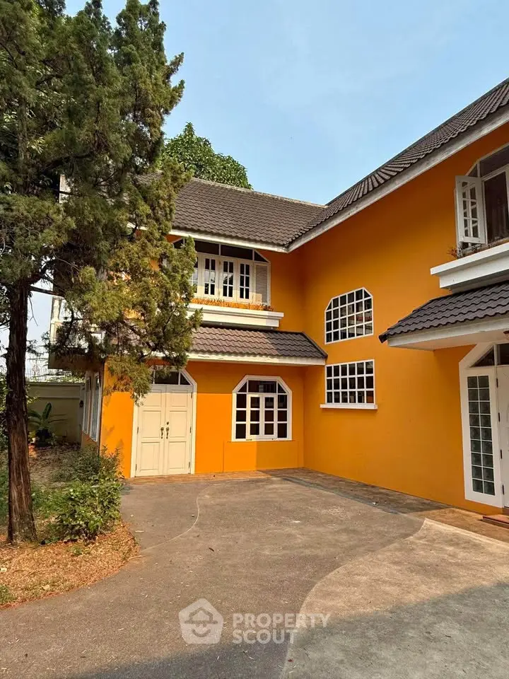 Charming orange house with unique windows and spacious driveway surrounded by greenery.