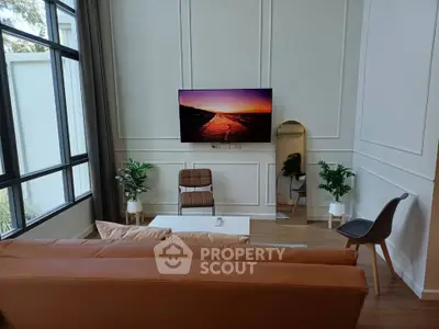 Modern living room with large windows, stylish furniture, and wall-mounted TV