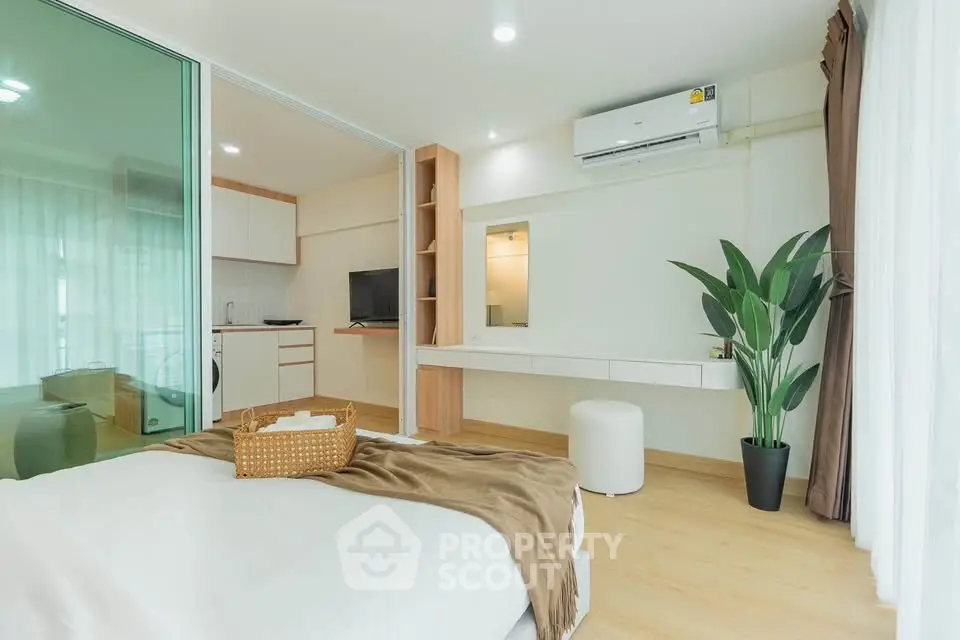 Modern bedroom with open layout, featuring a cozy bed, air conditioning, and a glimpse of a compact kitchen.