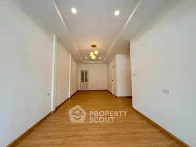 Spacious empty room with wooden flooring and modern lighting, perfect for customization.