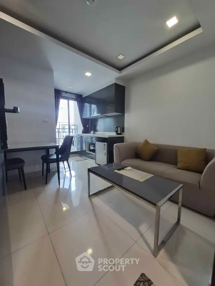 Modern living room with open kitchen and balcony view, featuring sleek furniture and contemporary design.