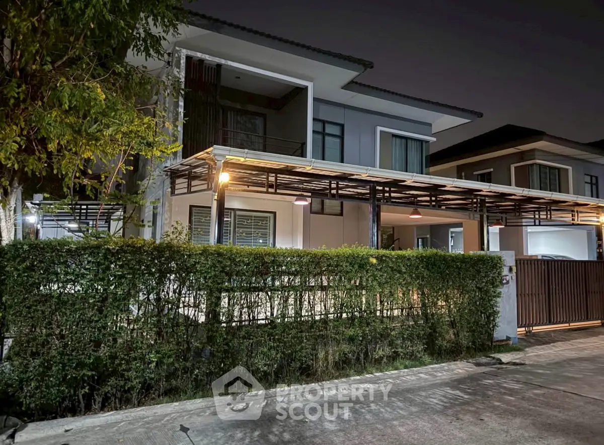 Modern two-story house with sleek design and well-lit exterior at night, featuring a spacious balcony and lush greenery.