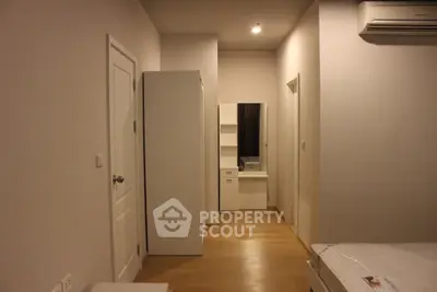 Modern bedroom with sleek white furniture and wooden flooring, featuring a minimalist design and air conditioning.