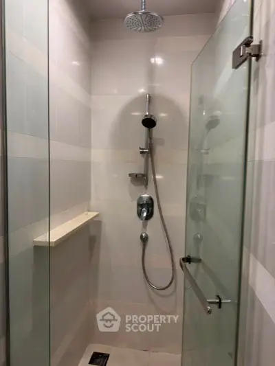 Modern shower area with glass door and rainfall showerhead in sleek bathroom design.
