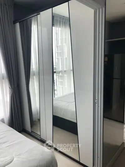 Modern bedroom with mirrored wardrobe and large windows in a stylish apartment.