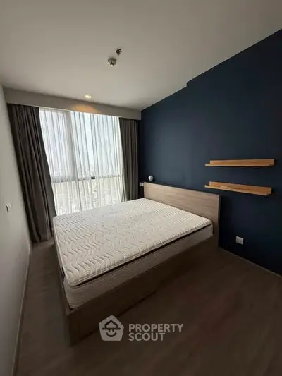 Modern bedroom with large window and stylish blue accent wall in a contemporary apartment.