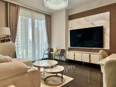Luxurious living room with elegant decor and large TV, featuring floor-to-ceiling windows and modern chandelier.