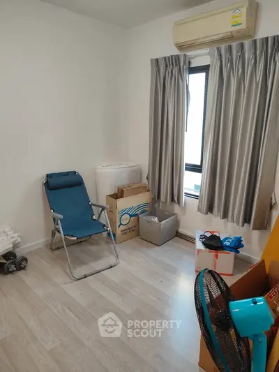 Cozy room with air conditioning, light wood flooring, and a window with curtains, ideal for a small office or study.