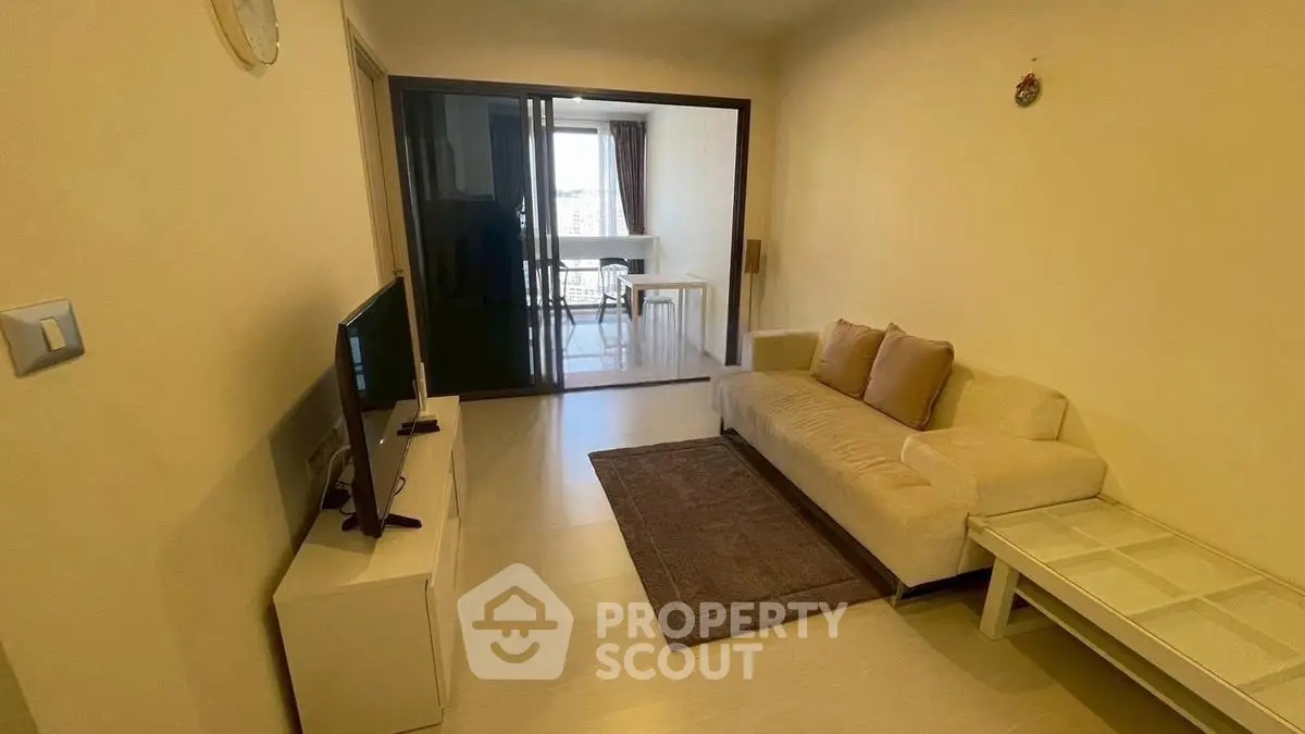 Cozy living room with modern sofa and TV, leading to a bright dining area.