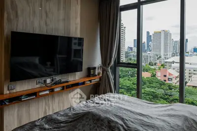 Modern bedroom with city view, featuring a wall-mounted TV and large windows for natural light.