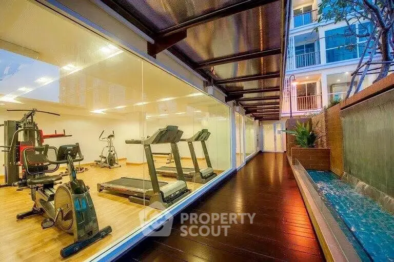 Modern gym with glass walls and adjacent water feature in luxury apartment complex.
