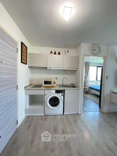 Modern compact kitchen with washing machine and microwave in a cozy apartment setting.