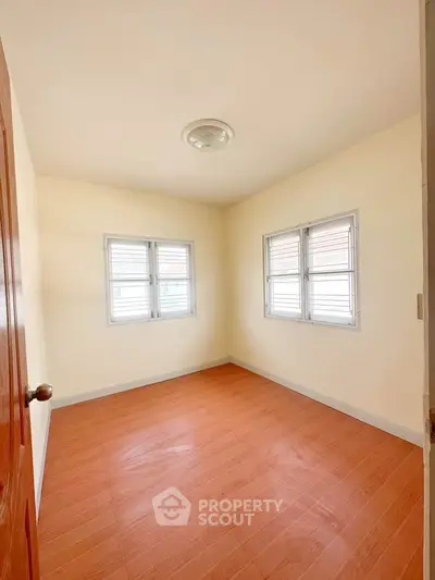Bright and airy bedroom with wooden flooring and ample natural light from two windows.