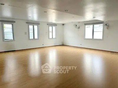 Spacious empty room with wooden flooring and ample natural light from multiple windows.