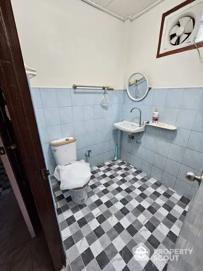 Compact bathroom with checkered floor tiles, wall-mounted sink, and classic white toilet, complemented by a small window for natural light.