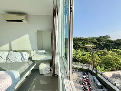 Bright bedroom with large window offering lush green view, modern furniture, and air conditioning.