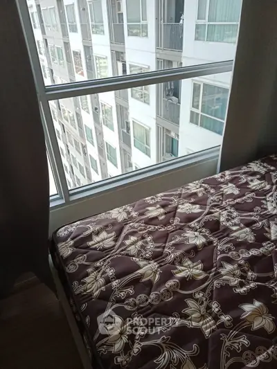 Cozy bedroom with large window offering city views in modern apartment building.