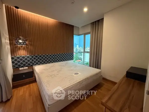 Modern bedroom with wooden flooring and large window offering city view.